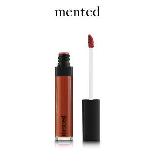 Image of a Mented Blood Orange Liquid Lipstick (2-Pack) from the Sangria Collection with the cap removed and standing beside it. The lipstick is a warm, brownish-red shade, and the applicator wand is visible. The word "mented" is written above the lipstick in black text.
