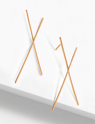 The Chopstick Earrings by Sonia Hou Jewelry feature a minimalist, asymmetrical design of thin gold rods overlapping each other, evoking the elegance of chopsticks. They are elegantly presented against a simple, white background.