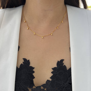 A close-up of a person wearing the Minimalist Rice Bead Chain Necklace by Sonia Hou Jewelry. The person is dressed in a white blazer over a black, lacy, floral-patterned top, revealing the necklace against their skin. This elegant piece subtly symbolizes wealth and good health.