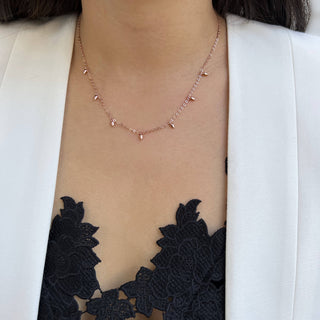 A close-up of a person wearing the Minimalist Rice Bead Chain Necklace by Sonia Hou Jewelry, featuring delicate drop-shaped pendants that symbolize wealth. They are dressed in a black lace top adorned with intricate floral patterns, layered under a chic white blazer.